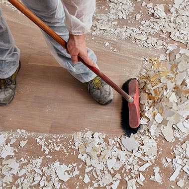 cleaning company in Nottingham, person sweeping plaster debris on a wooden floor.